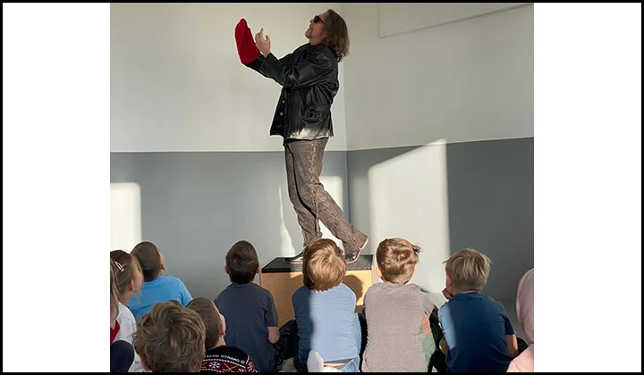 Felix Würgler, auf einem Tisch stehend - umgeben von Kindern, performed Norbert Nackendick von Michael Ende bei einer Kinderlesung.