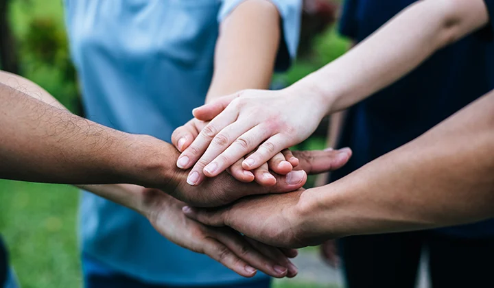 Menschen stehen im Kreis und haben die ausgestreckten Hände aufeinander gelegt.